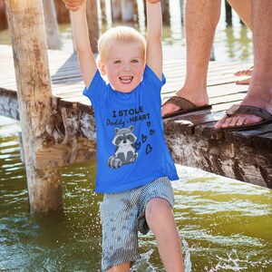 K&ouml;nnte beinhalten: Ein blaues T-Shirt mit einem Waschb&auml;r-Motiv und dem Text "Ich habe Papas Herz gestohlen".