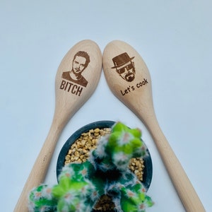 Puede incluir: Dos cucharas de madera con un personaje de la serie de televisión Breaking Bad en cada una. Una cuchara dice "Bitch" y la otra dice "Let's cook".