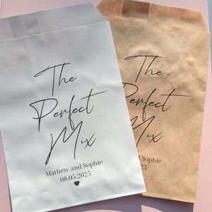 May include: Two paper favor bags, one white and one brown, with the text "The Perfect Mix" in elegant black script. The white bag includes names and a date. Suitable for weddings or special events.