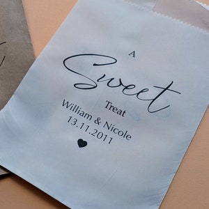 May include: A white paper bag with a black cursive inscription that reads "A Sweet Treat William & Nicole 13.11.2011" with a small black heart symbol below the date.
