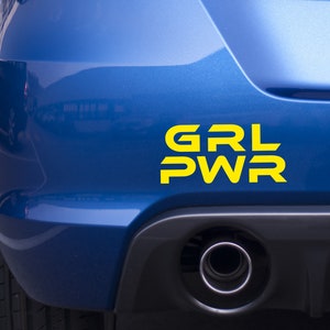 Op de afbeelding: Een blauwe auto met een gele vinyl sticker met de tekst "GRL PWR" op de achterbumper.