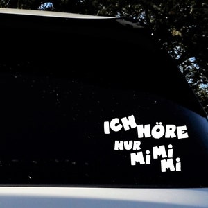 以下が含まれることがあります： 黒い車の窓に貼られた白いビニールステッカーに「Ich höre nur Mi Mi Mi」と書かれています。
