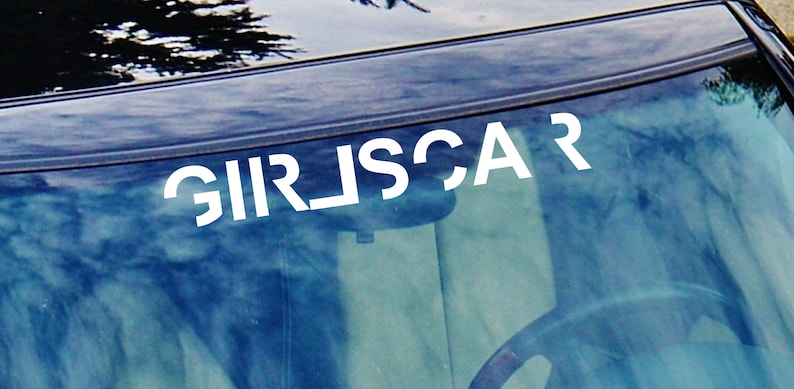 May include: A white vinyl decal with the text "GIRLSCAR" on a car windshield.