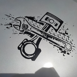 Puede incluir: Ilustración en blanco y negro de una llave inglesa y un pistón, con un efecto de pintura salpicada en el fondo.