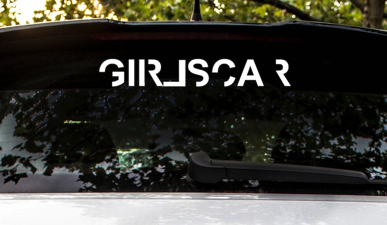 May include: A black car with a white vinyl decal on the rear window that reads "GIRLSCAR".