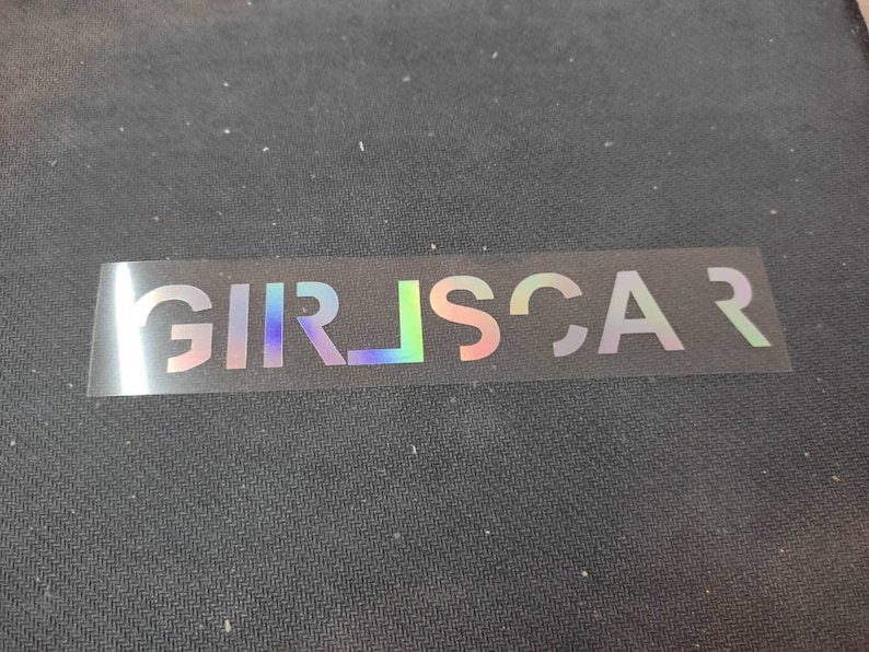 May include: A clear sticker with the iridescent text "GIRLSCAR" printed on it.