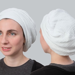 May include: White cotton turban style head covering. The fabric is soft and textured. The turban is worn on a person's head.