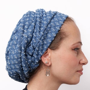May include: A blue denim head covering with a textured pattern. The head covering is worn with a black shirt and silver earrings. The earrings have a star stud and a dangling design with small silver elements.