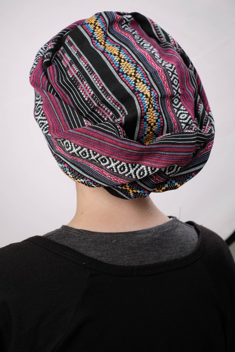 May include: A black, pink, blue, and yellow patterned turban style head wrap. The head wrap is made of a soft, woven fabric.