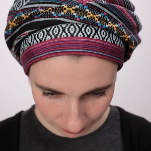 May include: A woman wearing a black and red patterned turban with a geometric design. The turban is made of a soft, woven fabric.