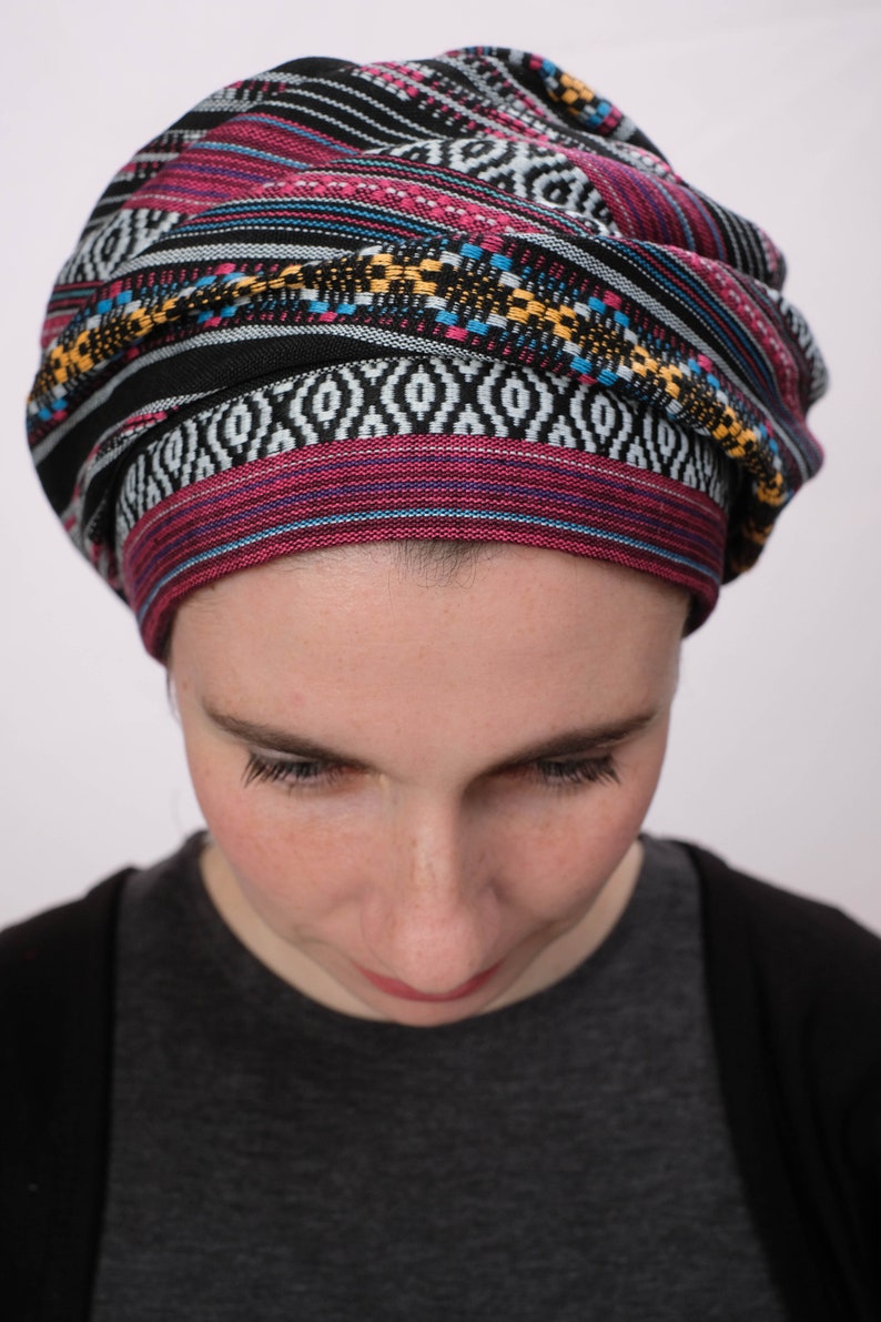 May include: A woman wearing a black and red patterned turban with a geometric design. The turban is made of a soft, woven fabric.