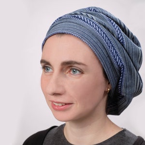 May include: A woman wearing a blue and white patterned head covering. The head covering is made of a soft, stretchy fabric and is tied in a knot at the back of the head.