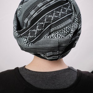 May include: A person wearing a black and white patterned turban. The turban is made of a soft, woven fabric.