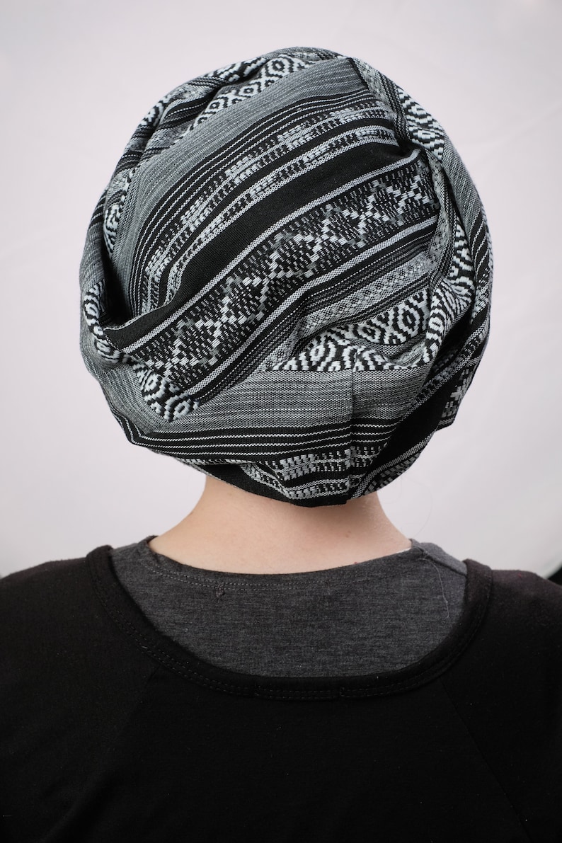 May include: A person wearing a black and white patterned turban. The turban is made of a soft, woven fabric.