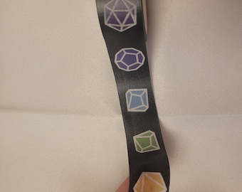 Könnte beinhalten: Schwarzes Washi-Tape mit farbenfrohen geometrischen Würfeldesigns. Die Würfel sind in Lila-, Blau-, Grün- und Gelbtönen gehalten. Oben auf dem Band befindet sich ein Sterndesign. Das Band ist wahrscheinlich zum Basteln oder Scrapbooking gedacht.