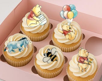 Puede incluir: Seis cupcakes en una caja rosa, cada uno cubierto con glaseado blanco y un personaje diferente de Winnie the Pooh. Los personajes incluyen a Pooh con miel, Ígor, una abeja y Pooh con globos. Los cupcakes están en una caja rosa.