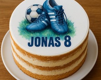 Puede incluir: Una tarta en capas con una parte superior blanca que presenta un balón de fútbol y botas de fútbol azules sobre hierba verde. La tarta tiene el nombre "JONAS" y el número "8" en azul.