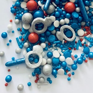 May include: A mix of blue, red, white, and silver sprinkles. The sprinkles are in the shape of stars, hearts, and other shapes.