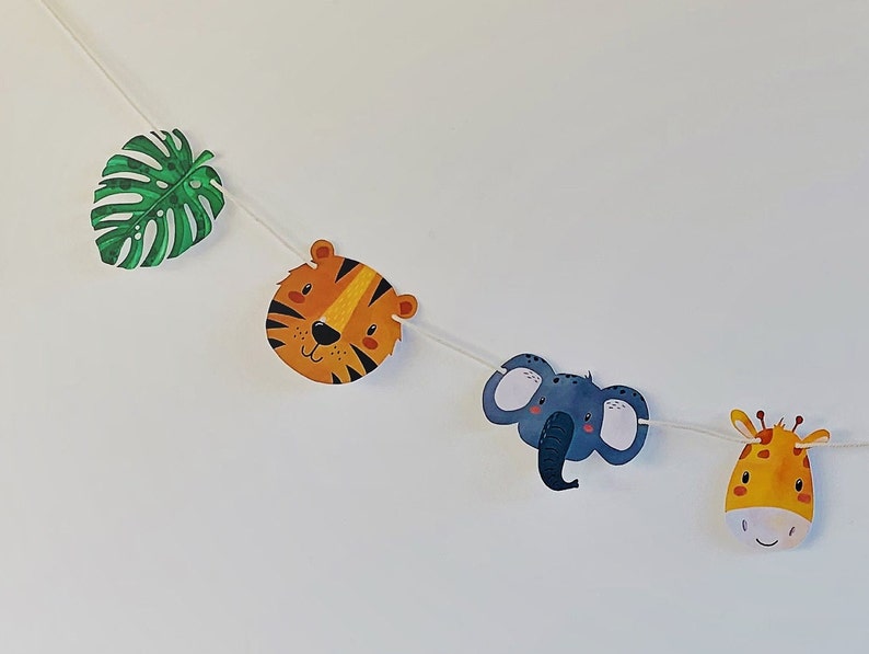 May include: A green leaf, a tiger face, a gray elephant face, and a yellow giraffe face are strung together on a white string. This is a jungle-themed party banner.