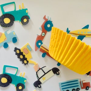 May include: Assortment of colorful vehicle-themed cupcake toppers, including a yellow construction truck, a blue and yellow airplane, a red race car, a yellow bulldozer, and two green tractors. The toppers are on a white background with a yellow cupcake liner.