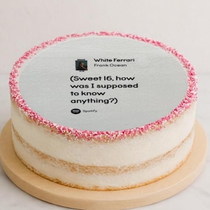Könnte beinhalten: Ein runder Kuchen mit weißem Zuckerguss und rosa Streuseln am Rand. Auf der Oberseite des Kuchens befindet sich eine Spotify-Grafik mit dem Text "White Ferrari Frank Ocean" und dem Text "(Sweet 16, how was I supposed to know anything?)". Der Kuchen steht auf einem hölzernen Kuchenständer.