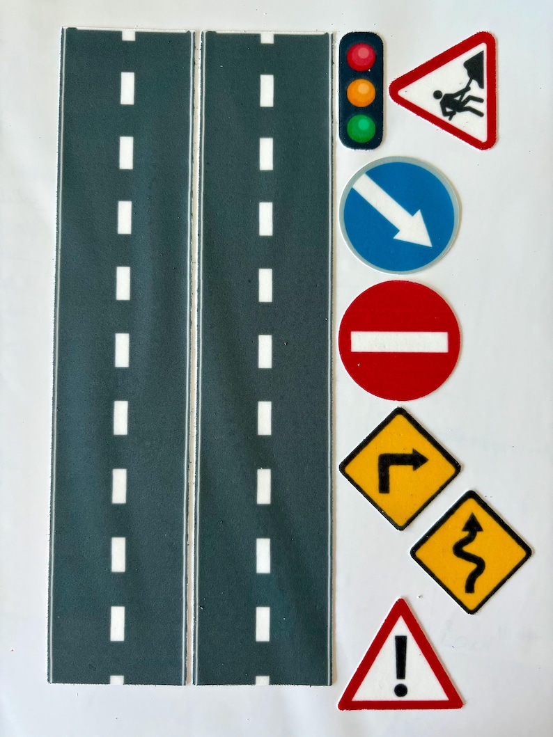 May include: A set of toy road pieces and traffic signs. The road pieces are dark gray with white dashed lines. Traffic signs include a stoplight, a yield sign, a do not enter sign, and several warning signs.
