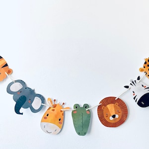 May include: A colorful garland with jungle animal faces, including a tiger, elephant, giraffe, frog, lion, and zebra, with green monstera leaves on either end.