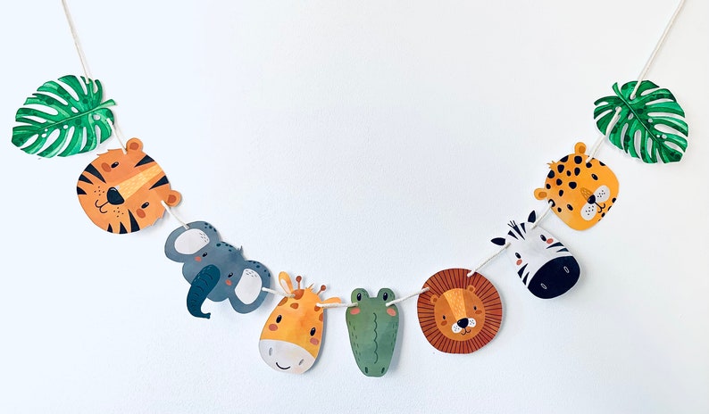 May include: A colorful garland with jungle animal faces, including a tiger, elephant, giraffe, frog, lion, and zebra, with green monstera leaves on either end.