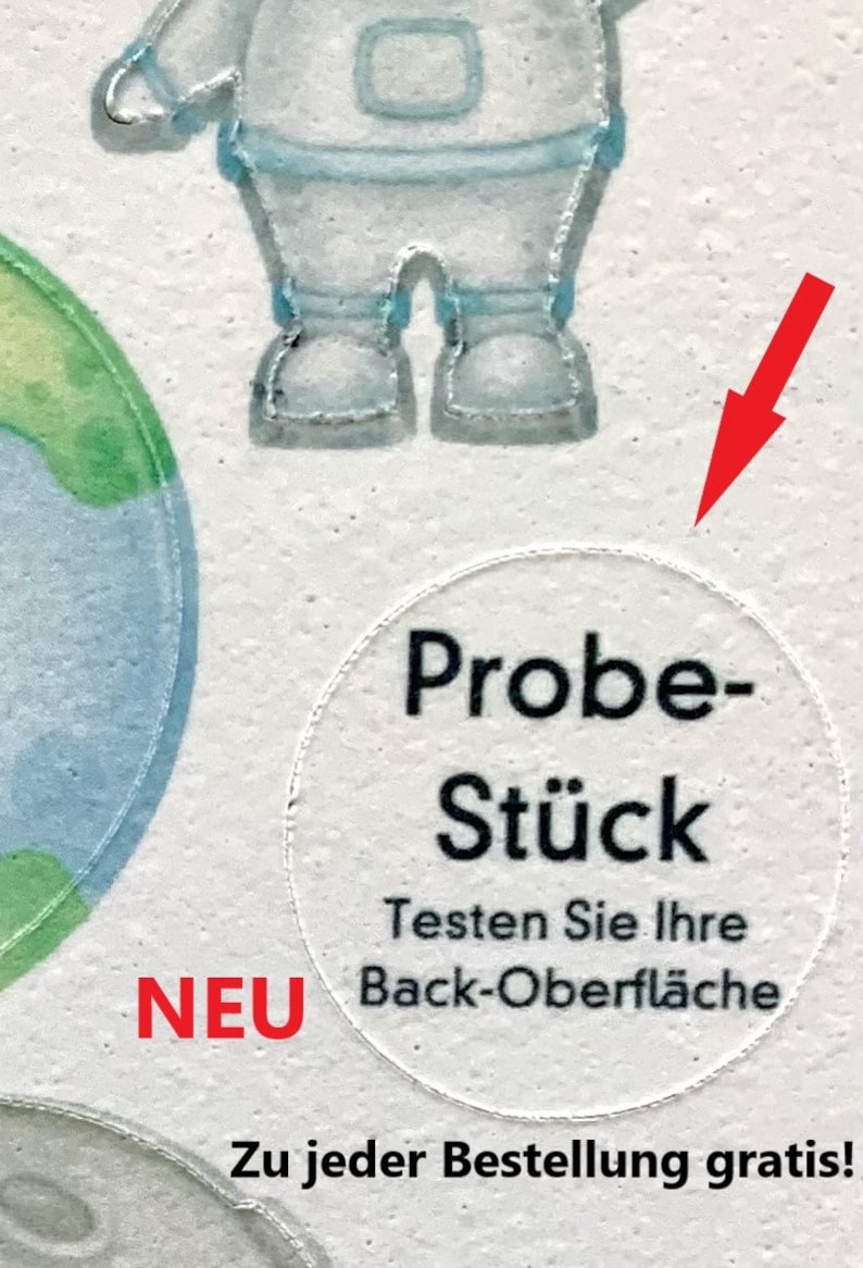 May include: A white circle sticker with black text that reads "Probe-St&uuml;ck" and "Testen Sie Ihre Back-Oberfl&auml;che". The sticker also has the word "NEU" in red text below it. The text below the sticker reads "Zu jeder Bestellung gratis!"