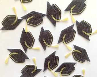 May include: A collection of black graduation caps with yellow tassels. The caps are scattered on a white background.