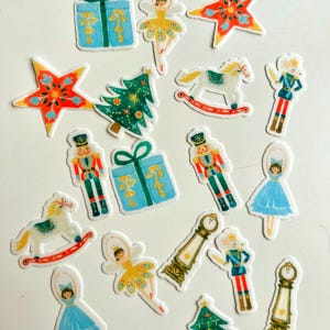 Könnte beinhalten: Eine Sammlung skurriler Aufkleber zum Thema Weihnachten. Die Aufkleber zeigen eine Vielzahl festlicher Designs, darunter Geschenkboxen, Ballerinas, Sterne, Weihnachtsbäume, Schaukelpferde, Nussknacker und ein Mäuse-Soldat.