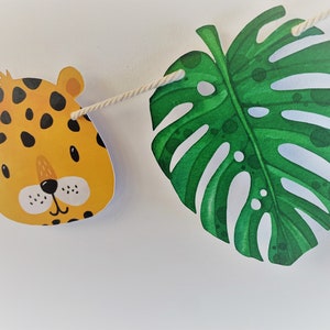 May include: A jungle-themed party banner with a yellow and black leopard print animal head and a green monstera leaf.