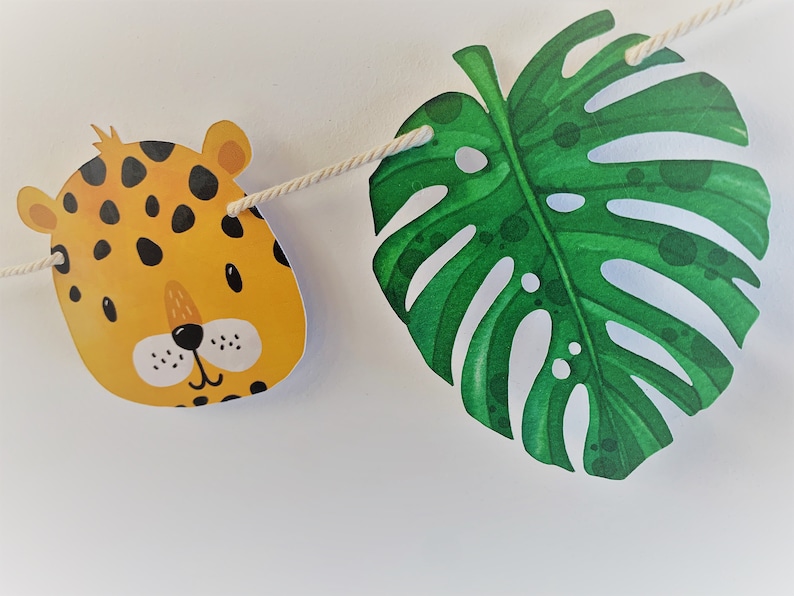 May include: A jungle-themed party banner with a yellow and black leopard print animal head and a green monstera leaf.