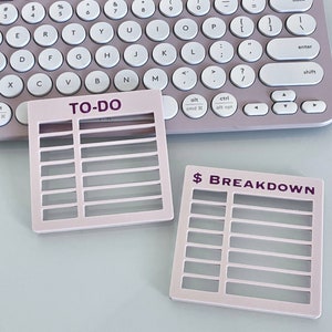 May include: Two pink to-do list organizers with grid sections. The top organizer has the text "TO-DO" in purple lettering. The bottom organizer has the text "$ BREAKDOWN" in purple lettering.