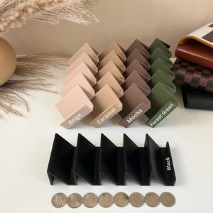 May include: A collection of angled display stands in various colors, including beige, caramel, mocha, and forest green, with the word "Black" on a black stand. A calculator and wallets are in the background.