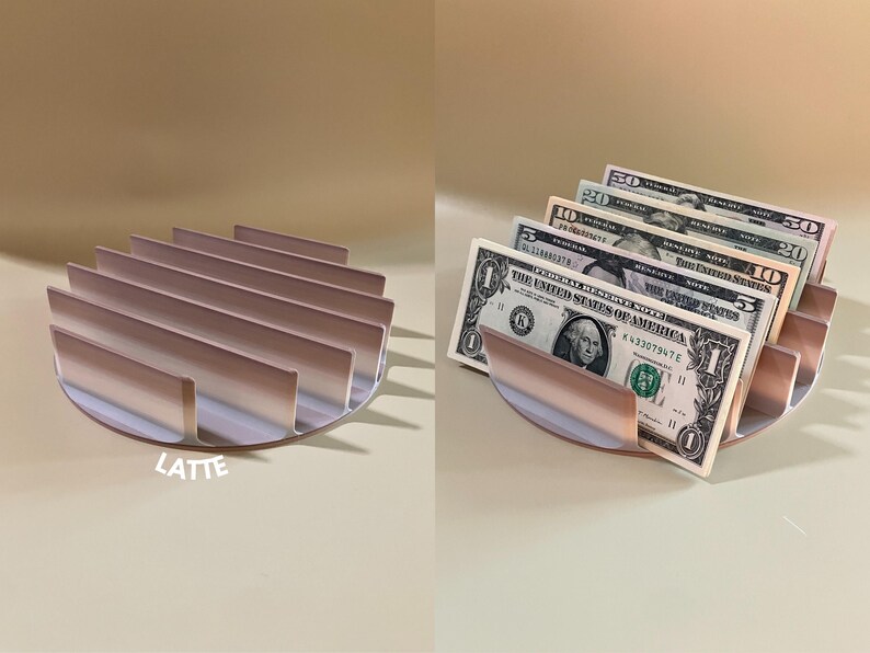 Puede incluir: Un organizador de efectivo de metal color oro rosa con un dise&ntilde;o curvo y m&uacute;ltiples ranuras para guardar billetes. El organizador est&aacute; lleno de billetes de d&oacute;lar estadounidense, incluyendo un billete de 1$, 5$, 10$, 20$ y 50$.