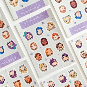 May include: Sheets of stickers featuring cartoon character portraits with various hair colors and styles. The stickers are arranged on light gray sheets with the text "STARDEWDLES" in a purple banner. Small purple floral accents are scattered around the stickers.