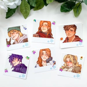 May include: A collection of six square art prints featuring illustrations of male characters in various outfits. Each print has a white border and is decorated with small floral and snowflake accents. The characters have different hair colors and expressions.