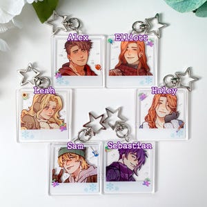 May include: Clear acrylic keychains featuring character portraits. Each keychain has a silver star-shaped charm and a metal ring. The portraits include Alex, Elliott, Leah, Haley, Sam, and Sebastian, with their names printed above.