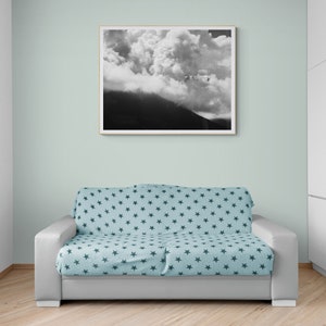 Puede incluir: Una fotograf&iacute;a en blanco y negro enmarcada de una monta&ntilde;a y nubes cuelga sobre un sof&aacute; gris. El sof&aacute; est&aacute; cubierto con una manta azul claro estampada con estrellas azul oscuro. La habitaci&oacute;n tiene paredes verde claro y suelo de madera.