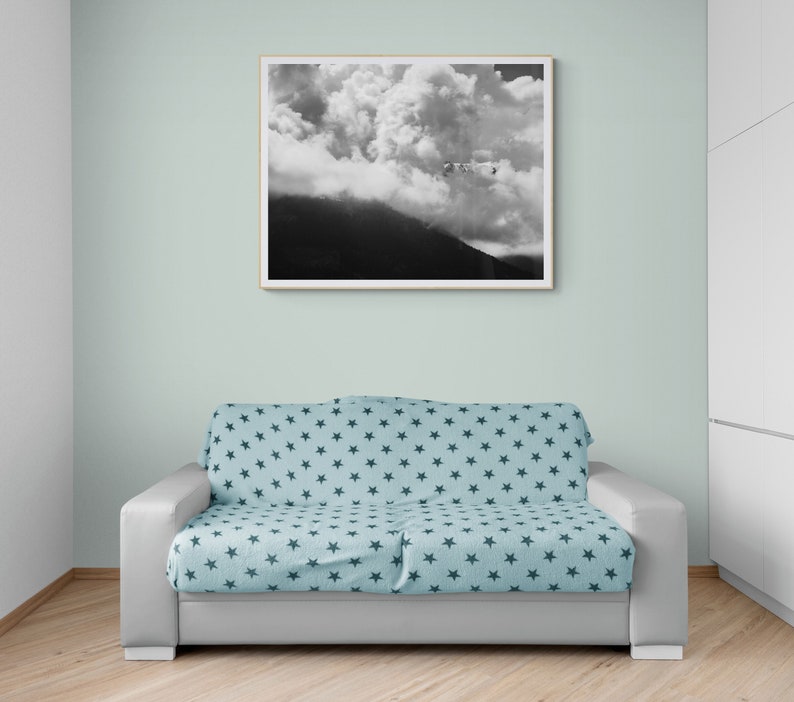 Puede incluir: Una fotograf&iacute;a en blanco y negro enmarcada de una monta&ntilde;a y nubes cuelga sobre un sof&aacute; gris. El sof&aacute; est&aacute; cubierto con una manta azul claro estampada con estrellas azul oscuro. La habitaci&oacute;n tiene paredes verde claro y suelo de madera.