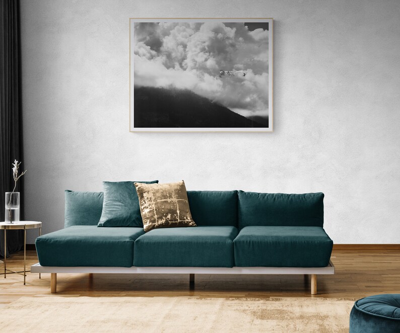 Puede incluir: Una fotograf&iacute;a en blanco y negro enmarcada de una cordillera nublada cuelga sobre un sof&aacute; seccional verde azulado. El sof&aacute; tiene varias almohadas, incluida una dorada con lentejuelas. A la izquierda hay una peque&ntilde;a mesa auxiliar con un jarr&oacute;n de cristal.