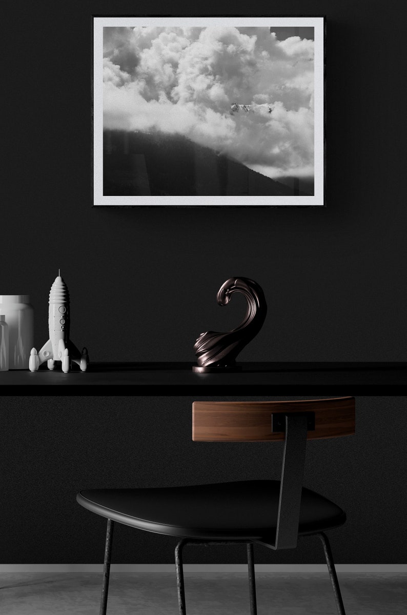 Puede incluir: Una impresi&oacute;n enmarcada en blanco y negro de una escena de monta&ntilde;a con nubes cuelga sobre una estanter&iacute;a negra. En la estanter&iacute;a hay una figura de cohete blanca y una escultura de onda de bronce oscuro. Una silla negra con respaldo de madera est&aacute; en primer plano.