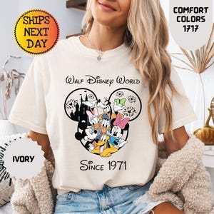 Pode incluir: Camiseta cor marfim com um gr&aacute;fico do Mickey Mouse e amigos, e o texto "Walt Disney World Since 1971". A camisa tem gola redonda e mangas curtas. A camisa tamb&eacute;m tem o texto "Comfort Colors 1717" e "Enviamos no dia seguinte".