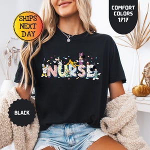 May include: Black t-shirt with the word "NURSE" in colorful, cartoon-style letters. The letters are decorated with images of cartoon characters. The shirt has a crew neck and short sleeves. The shirt also has the text "COMFORT COLORS 1717".