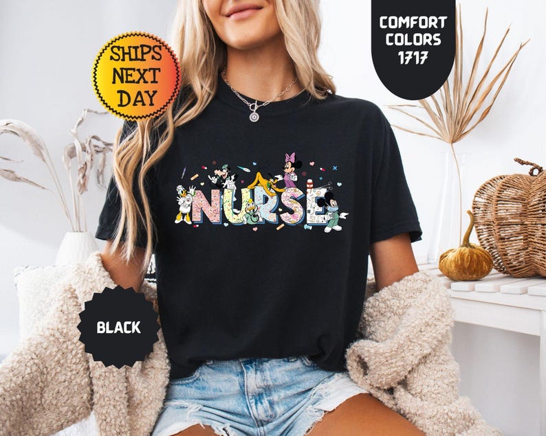 May include: Black t-shirt with the word "NURSE" in colorful, cartoon-style letters. The letters are decorated with images of cartoon characters. The shirt has a crew neck and short sleeves. The shirt also has the text "COMFORT COLORS 1717".