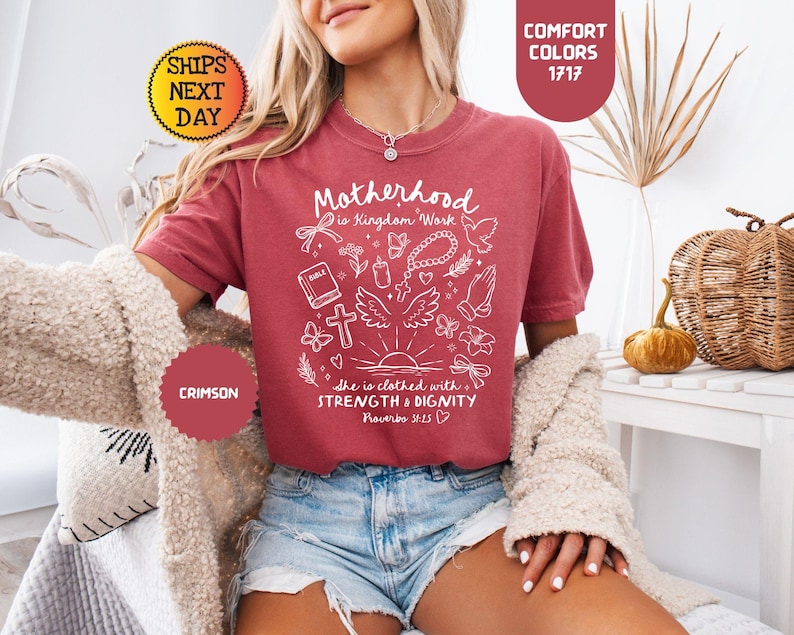 May include: Crimson-colored t-shirt with the text "Motherhood is Kingdom Work" and other religious symbols in white. The shirt also has the text "She is clothed with STRENGTH & DIGNITY Proverbs 31:25".