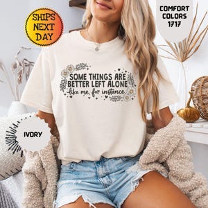 May include: Ivory-colored t-shirt with the text "SOME THINGS ARE BETTER LEFT ALONE like me, for instance" in black script and floral accents. The shirt is part of the Comfort Colors collection.