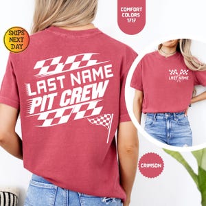 May include: Red t-shirt with white text that says "Last Name Pit Crew" and a checkered flag design. The shirt is shown on a model wearing blue jeans.