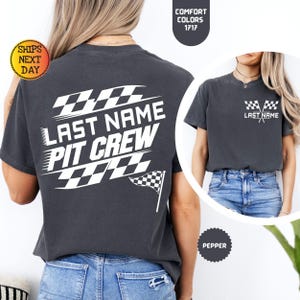 May include: A dark gray t-shirt with a white design on the back that says "Last Name Pit Crew" with a checkered flag design. The front of the shirt has a smaller checkered flag design with the text "Last Name".